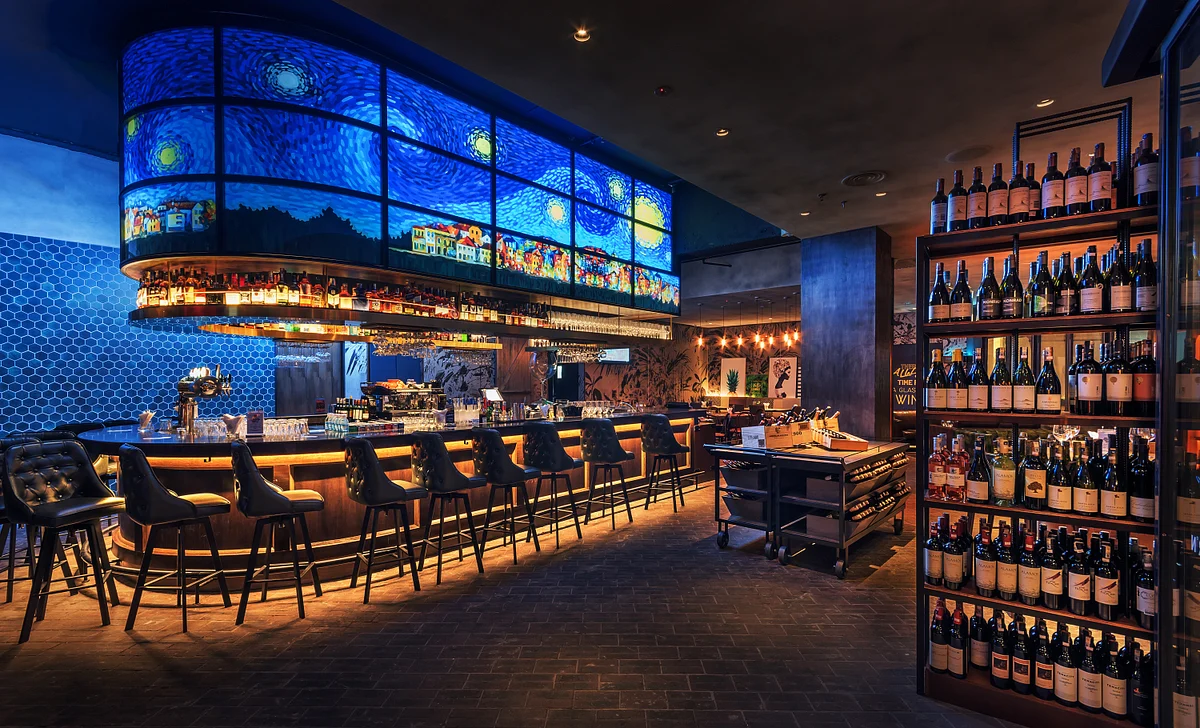 Stylish bar interior with blue illuminated ceiling, counter seating, and shelves of wine bottles