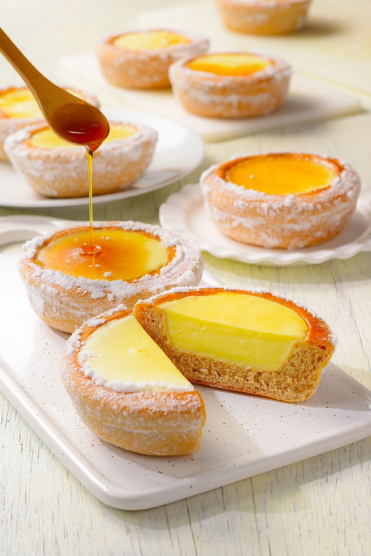 Custard tarts on a serving plate, including one cut open, with syrup drizzled from a spoon