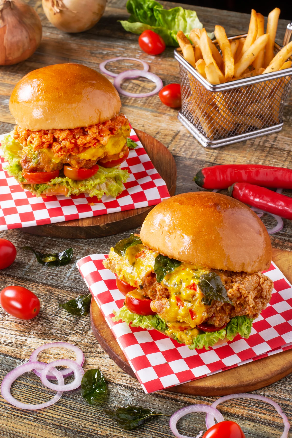 Two fried chicken burgers with lettuce, tomatoes, melted cheese, and fries