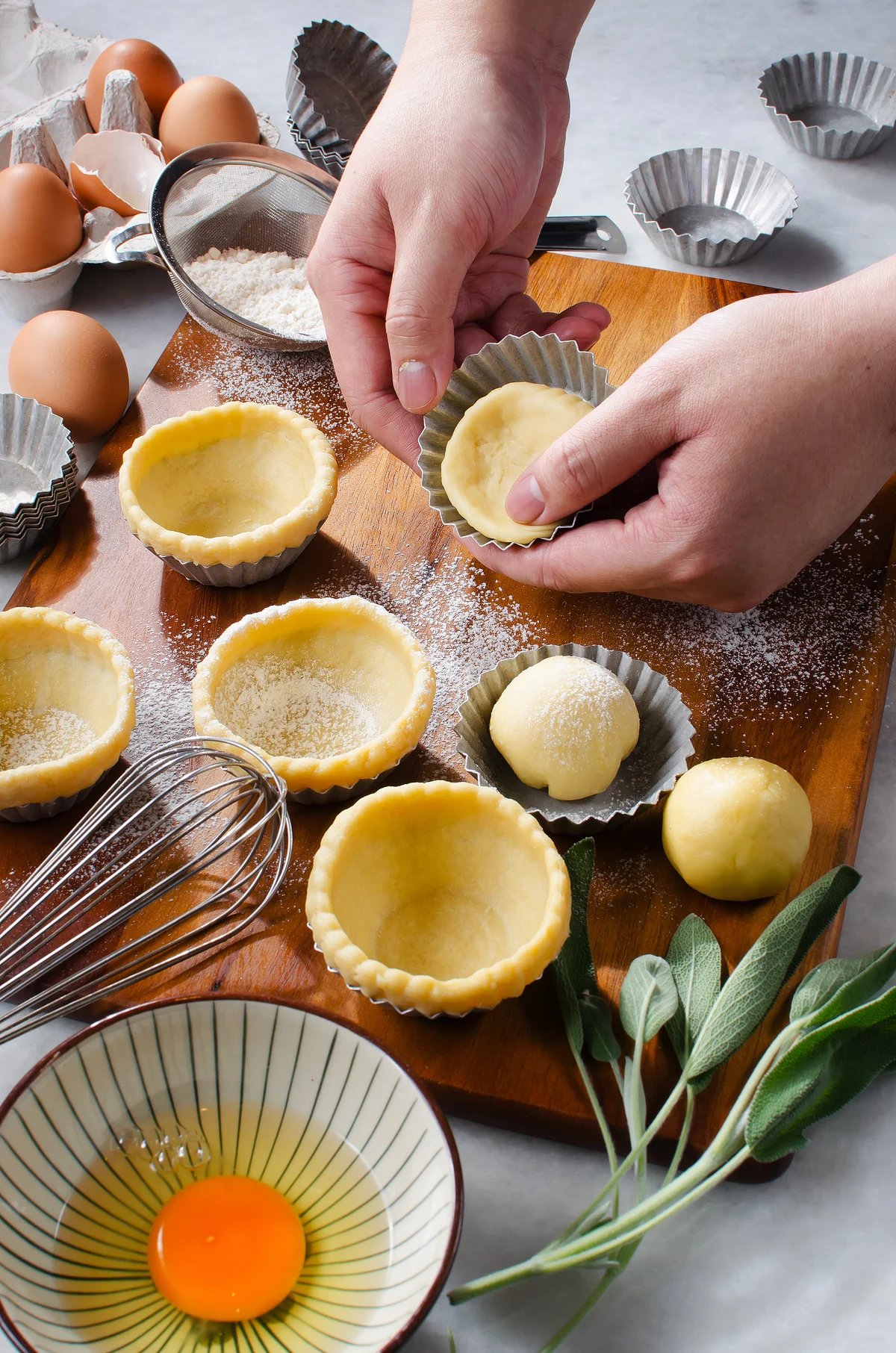Hands shaping pastry dough into tart shells on a floured wooden board