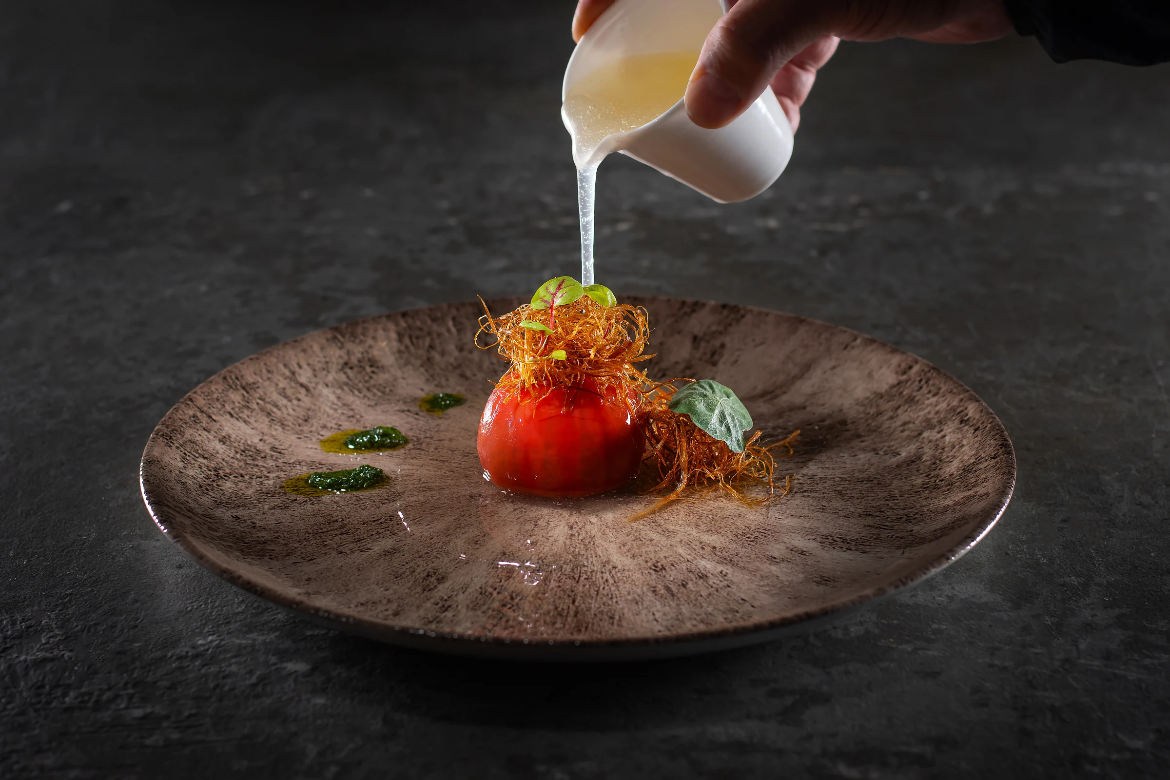 White sauce poured over a plated red tomato with crispy golden garnish and green herbs