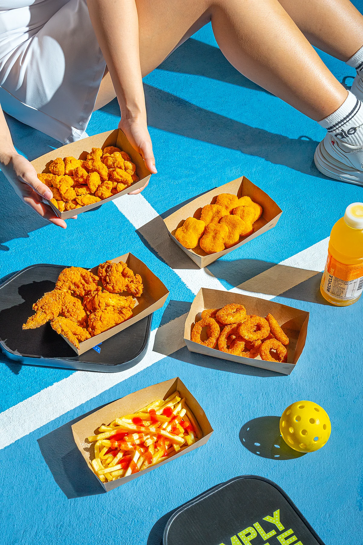 Fried chicken, nuggets, wings, onion rings and fries arranged on a blue court for a QSR campaign