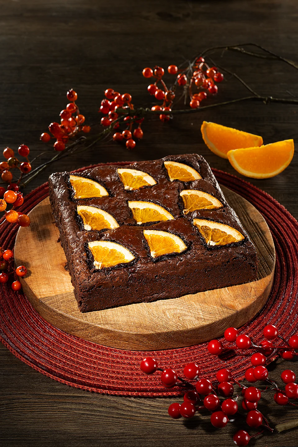 Square chocolate cake topped with orange slices on a wooden board