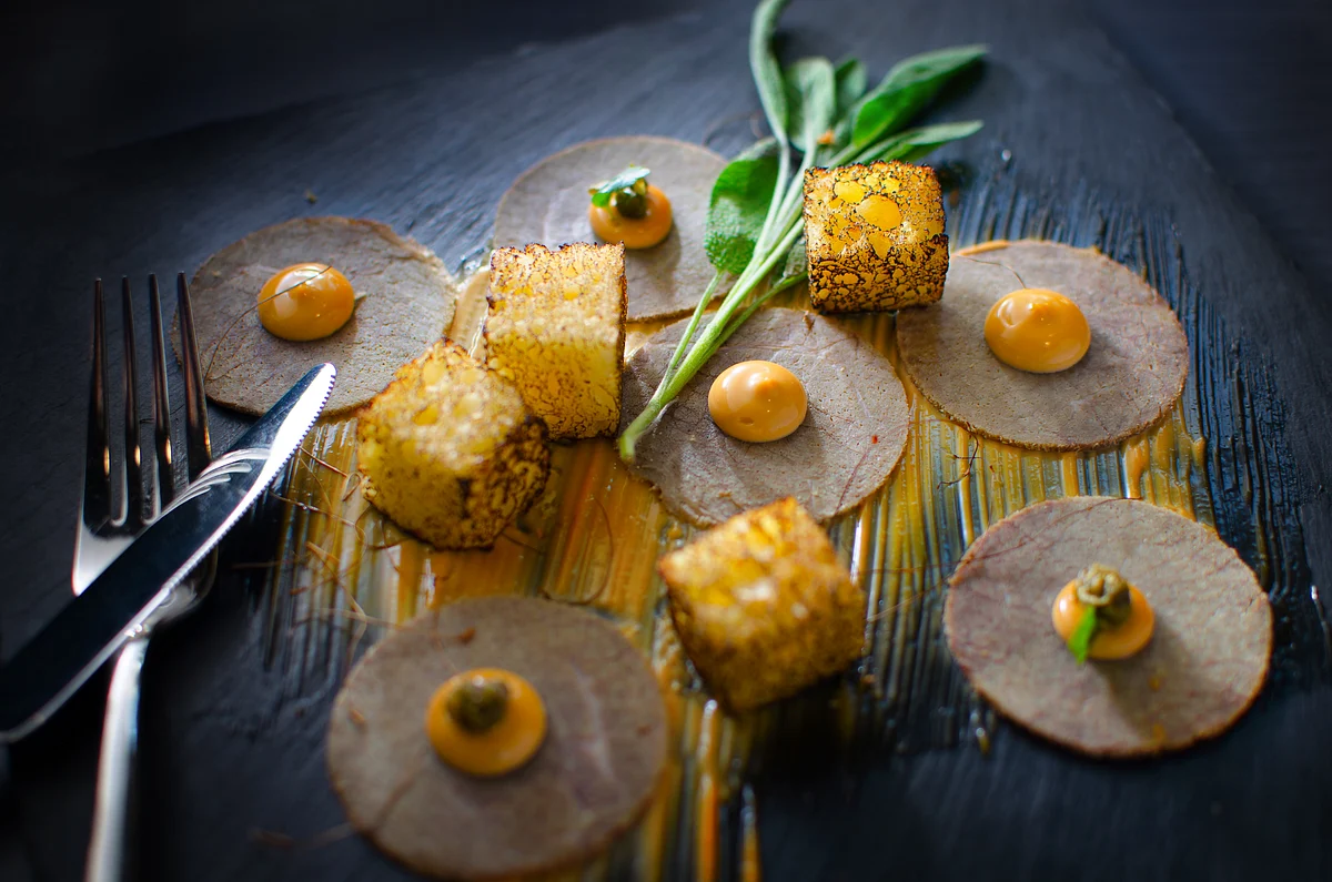 Fine-dining Western plate with sliced terrine, toasted croutons, sage, and carrot purée on dark slate.