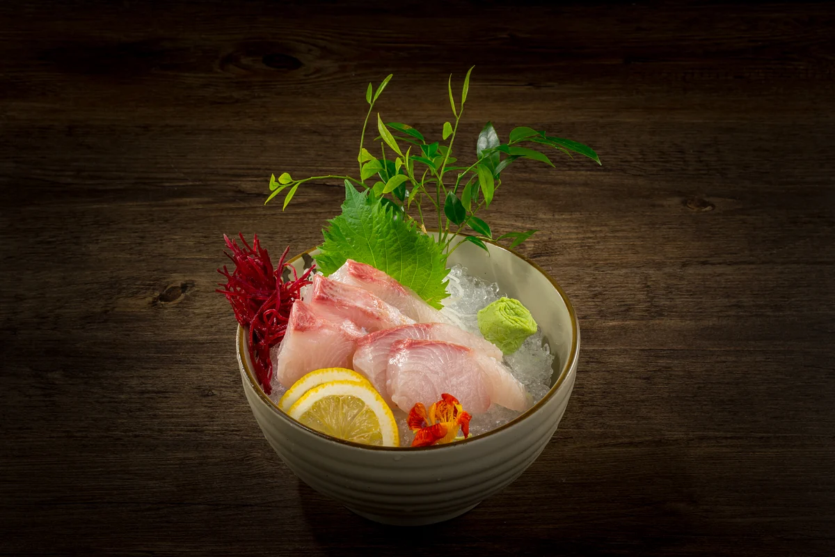 Sashimi slices with shiso, wasabi and lemon on crushed ice in a ceramic bowl