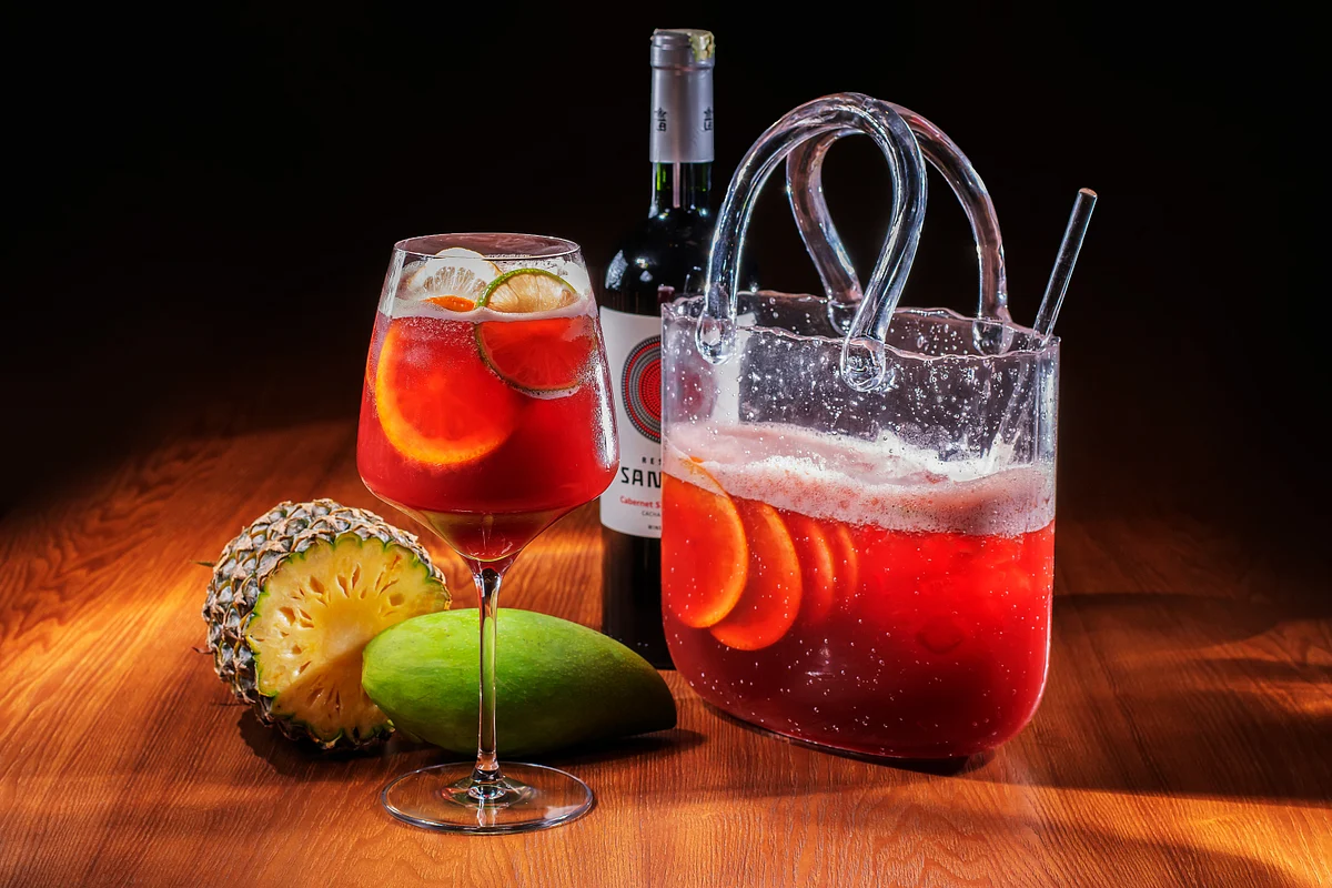 Red citrus punch in a clear pitcher and wine glass with pineapple and tropical fruit