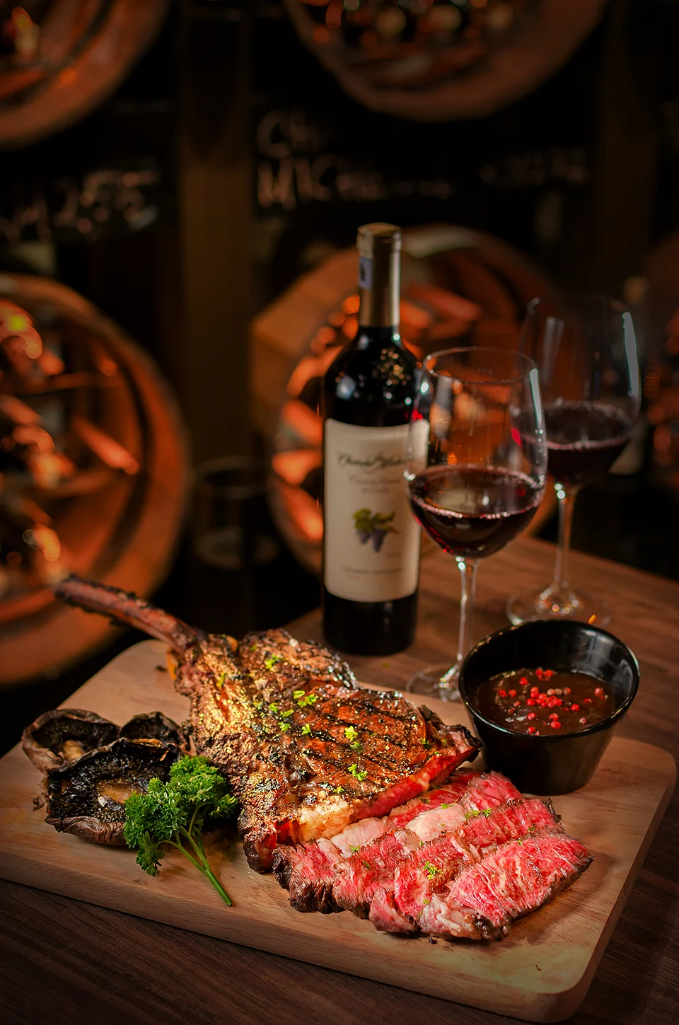 Tomahawk steak sliced medium-rare with roasted mushrooms, red wine and peppercorn sauce on a wooden board